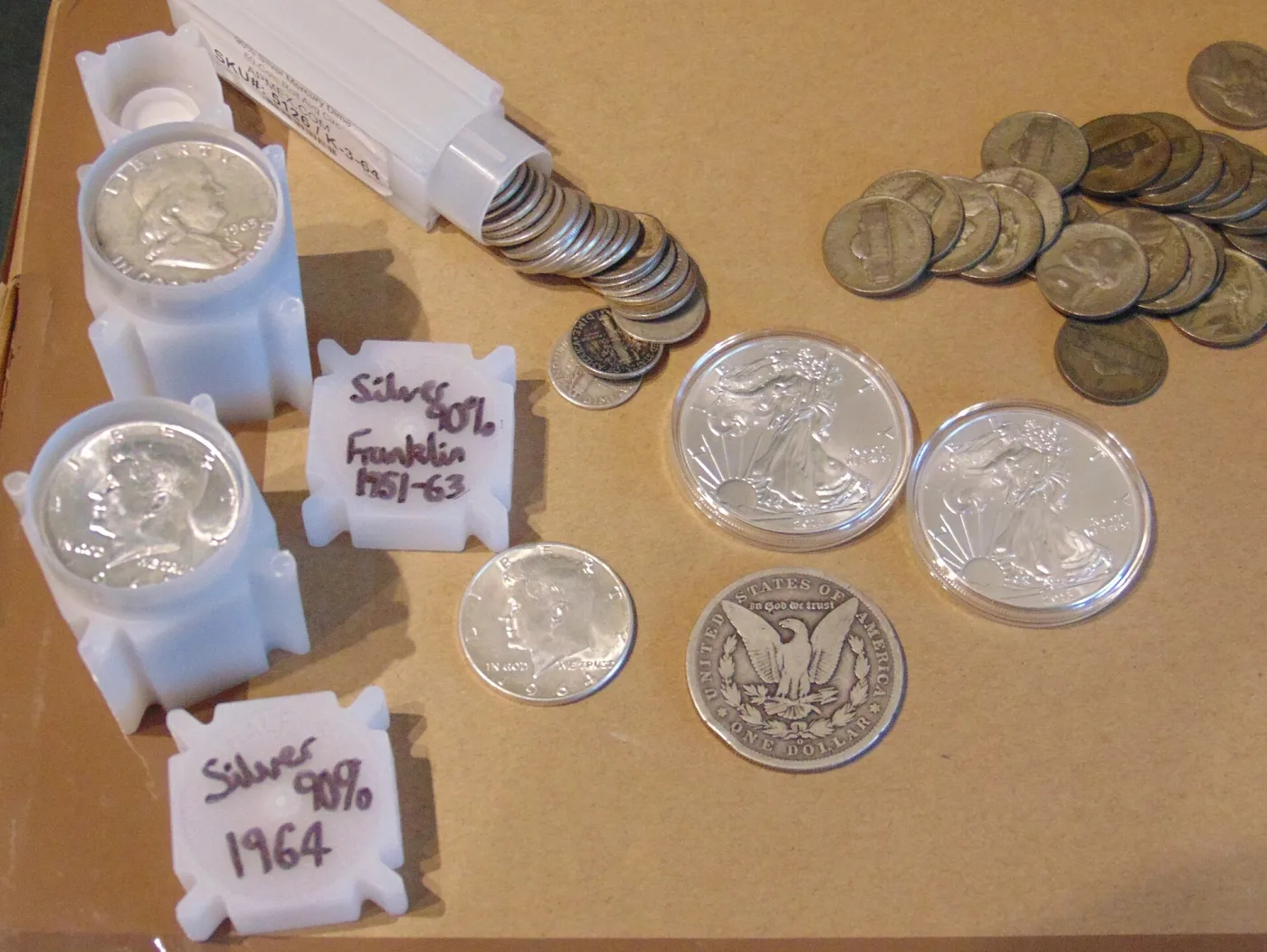 Two encapsulated American Silver Eagles laid out beside rolls of Franklin and Kennedy half dollars, loose Mercury dimes, a Morgan dollar and war nickels