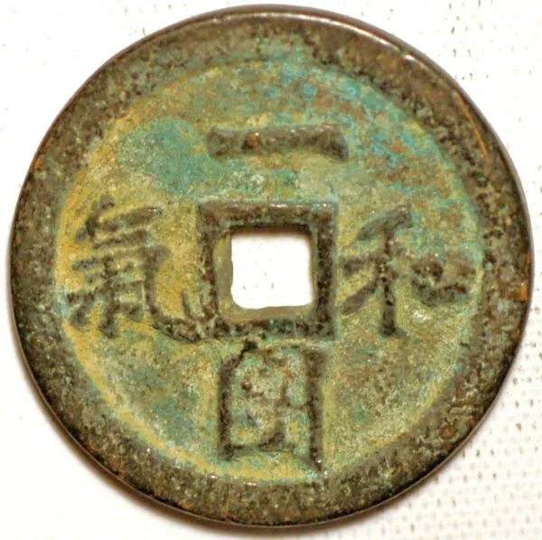 A round bronze object with a square central hole and four large Chinese characters around it, heavily patinated green and gold