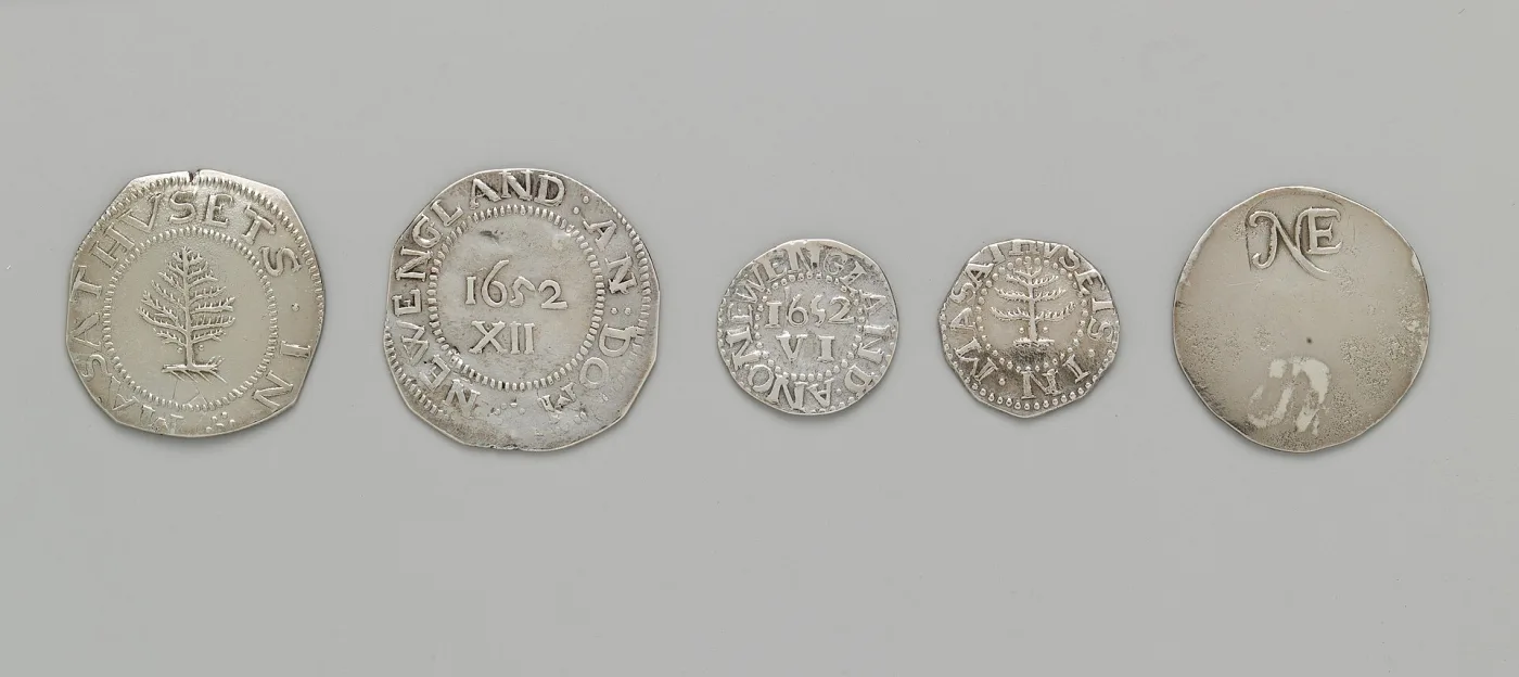 Five Massachusetts silver coins of 1652 laid in a row: a Pine Tree shilling obverse and reverse, a sixpence, a threepence and an NE-stamped shilling