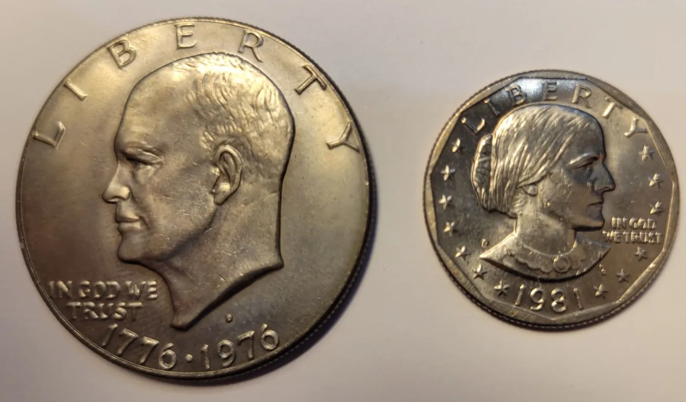 A Bicentennial Eisenhower dollar lying beside a much smaller 1981 Susan B. Anthony dollar for scale