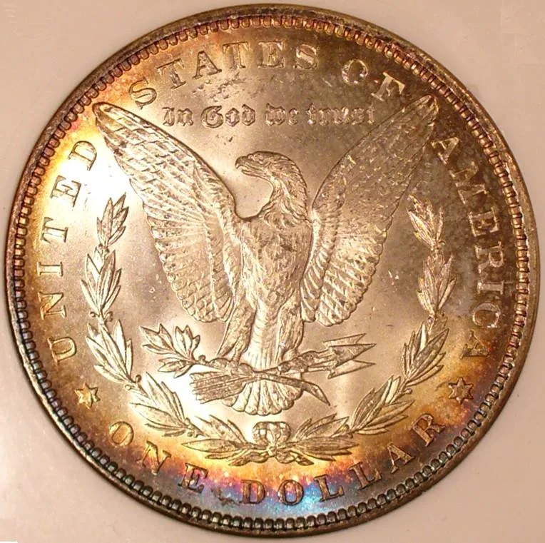 Reverse of an 1899 Morgan silver dollar inside a grading holder, its centre untoned and a band of amber, violet and blue colour ringing the rim