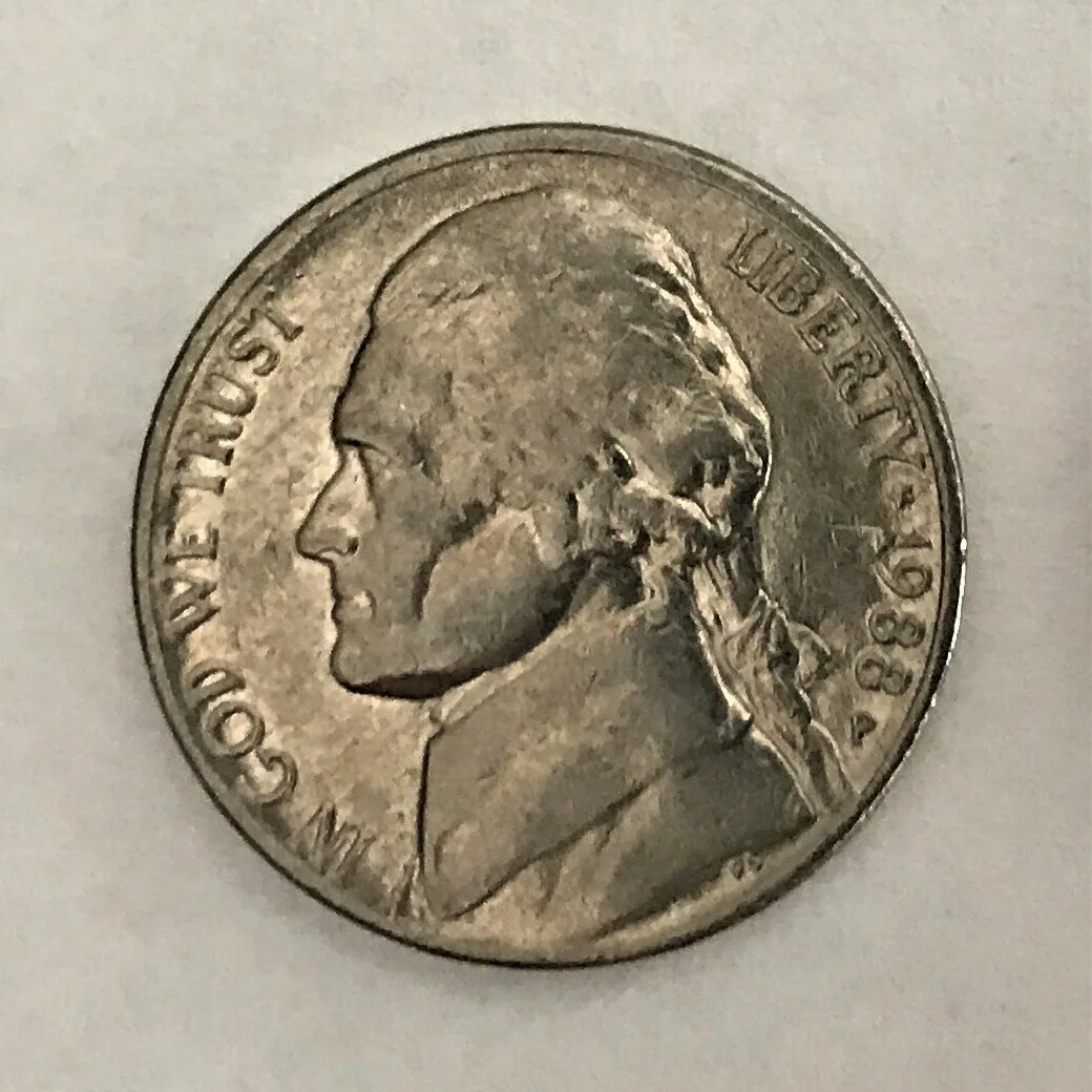 Obverse of a circulated 1988 Jefferson nickel with the hair above the ear and the cheekbone worn smooth while the lettering and date remain sharp