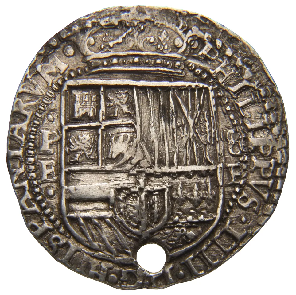 Obverse of an irregular hammered silver coin, the crowned quartered Spanish shield off-centre on a lumpy oval flan with a hole punched through it
